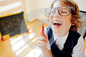 Cheerful little student bespectacled sits at school desk.