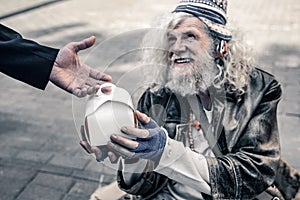 Cheerful long-haired old man living on the street and holding box with food