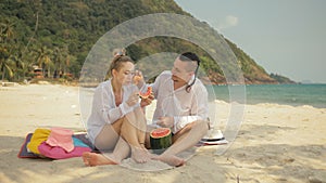 The cheerful love couple holding and eating slices of watermelon on tropical sand beach sea. Romantic lovers two people