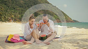 The cheerful love couple holding and eating slices of watermelon on tropical sand beach sea. Romantic lovers two people