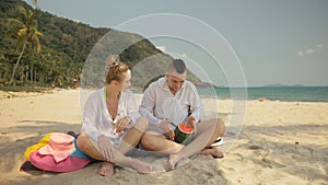 The cheerful love couple holding and eating slices of watermelon on tropical sand beach sea. Romantic lovers two people