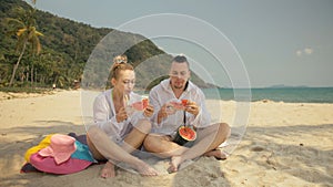 The cheerful love couple holding and eating slices of watermelon on tropical sand beach sea. Romantic lovers two people