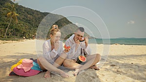 The cheerful love couple holding and eating slices of watermelon on tropical sand beach sea. Romantic lovers two people