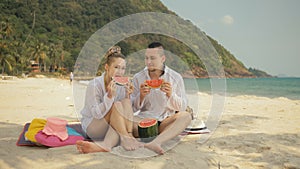 The cheerful love couple holding and eating slices of watermelon on tropical sand beach sea. Romantic lovers two people