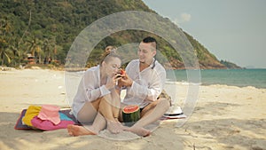 The cheerful love couple holding and eating slices of watermelon on tropical sand beach sea. Romantic lovers two people