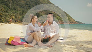 The cheerful love couple holding and eating slices of watermelon on tropical sand beach sea. Romantic lovers two people