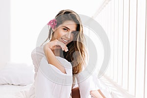 Cheerful lovely girl with amazing smile and romantic hairstyle gladly posing in white room. Portrait of cute young woman