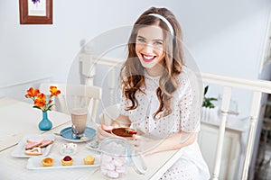 Cheerful lovely young woman eating dessert in cafe