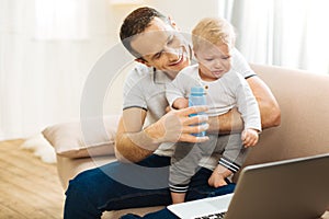 Cheerful loving father giving a bottle of water to his crying child