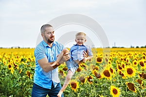 Cheerful loving father with his son on vacation in the field with sunflowers