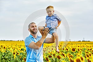 Cheerful loving father with his son on vacation in the field with sunflowers