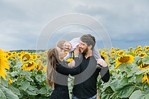 Cheerful loving young family with their son on vacation in a field with sunflowers