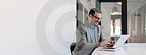 Cheerful male businessman entrepreneur professional working on laptop while sitting at office desk