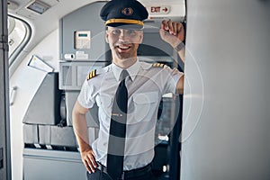 Cheerful male captain standing inside commercial airplane