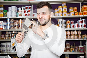cheerful male customer examining various types of brushes in paint store