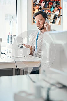 Cheerful male fashion designer speaking on cell phone at work