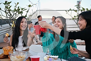 Cheerful male and female friends enjoying happy hour at terrace party and toasting drinks.