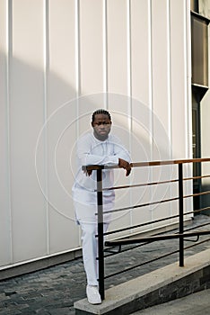 Cheerful male tourist dress in white wear dashiki ethnic smiling at city street on stairs. African American travel model
