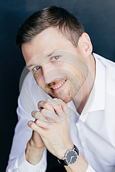 Cheerful male worker, friendly smile, palms together under chin, watch on hand, happy gaze. Professional portrait