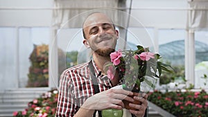 A cheerful man with a beard holds a pot of hands and wittily poses on the camera.