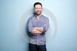 Cheerful man with beard posing against blue wall with arms crossed