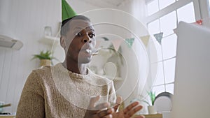 Cheerful man with birthday cap talks via videocall on laptop