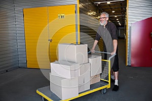 Cheerful man is carrying lot of boxes on cargo cart