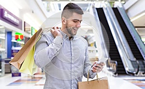 Cheerful man chatting on cellphone in shopping mall