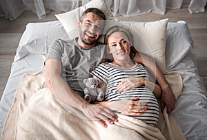 Cheerful man embracing pregnant woman on bed