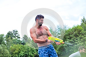 Cheerful man enjoying with squirt guns on pier during summer