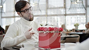 Cheerful man gives a big box full of flowers to his wife while sitting in a cafe