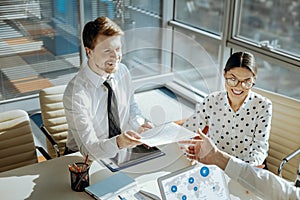 Cheerful man giving questionnaires to his colleague during meeting