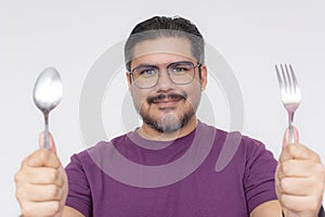 Cheerful man with glasses holding a fork and spoon with eagerness, portraying readiness for dining or mealtime