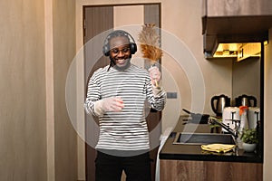 Cheerful man in headphone enjoying domestic chores, cleaning up his house and singing