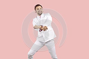Cheerful man in headphones listens to music and dances in gangnam style on pink background.