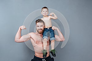 Cheerful man holding little son on shoulder and showing biceps