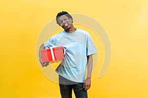 Cheerful Man Holding Red Gift Box On Yellow Background