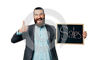 Cheerful man is holding thumb up and a blackboard with word sales on it.