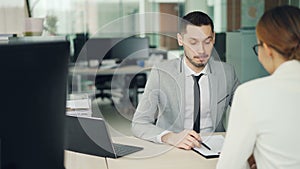 Cheerful man interviewer is talking to female candidate for job vacancy sitting at desk in modern office, smiling and