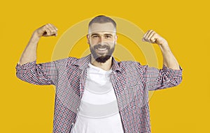 Cheerful man jokingly shows biceps demonstrating his strength on orange background.