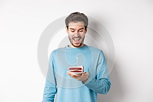 Cheerful man looking happy at birthday cake, celebrating bday, standing over white background