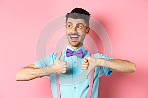 Cheerful man looking happy left, showing thumbs up down, judging product, give positive and negative feedback, standing