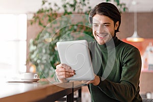 Cheerful man making video call via digital tablet, cafe interior