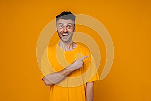 Cheerful man pointing finger away at copy space isolated over yellow wall