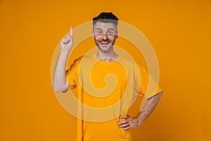 Cheerful man in pointing finger away at copy space isolated over yellow wall