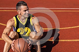 Cheerful man resting sitting on the basketball court after playing game.