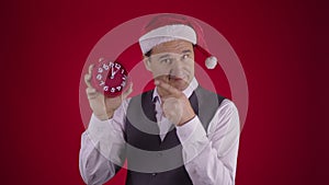 Cheerful man in Santa hat pointing at clock reminds minutes before New Year Eve