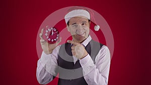 Cheerful man in Santa hat pointing at clock reminds Minutes before New Year Eve