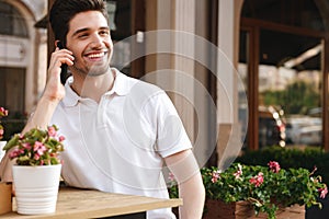 Cheerful man sitting in cafe outdoors while talking by mobile phone.