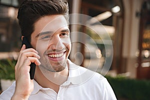 Cheerful man sitting in cafe outdoors while talking by mobile phone.